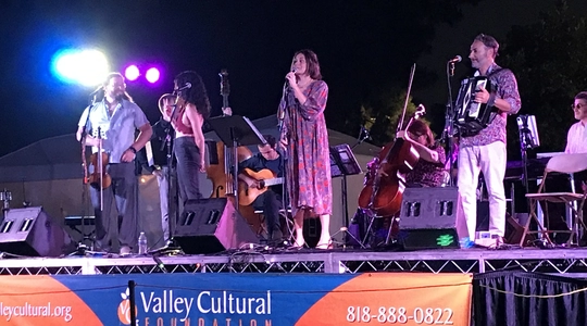 A photograph of the Element Band, male and female musicians performing against a night sky on a stage in North Hollywood Park