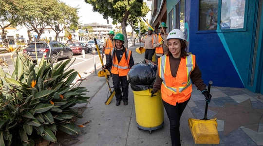 Los Angeles Conservation Corps members carrying cleaning supplies on a busy sidewalk 