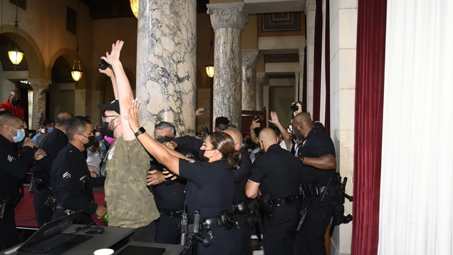 Demonstrator raises arms as he is arrested by police in City Council Chamber.